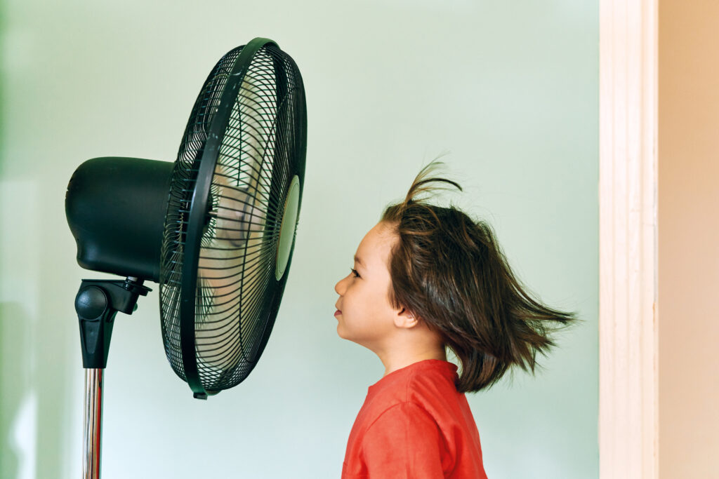 Child cools off in front of a house fan.