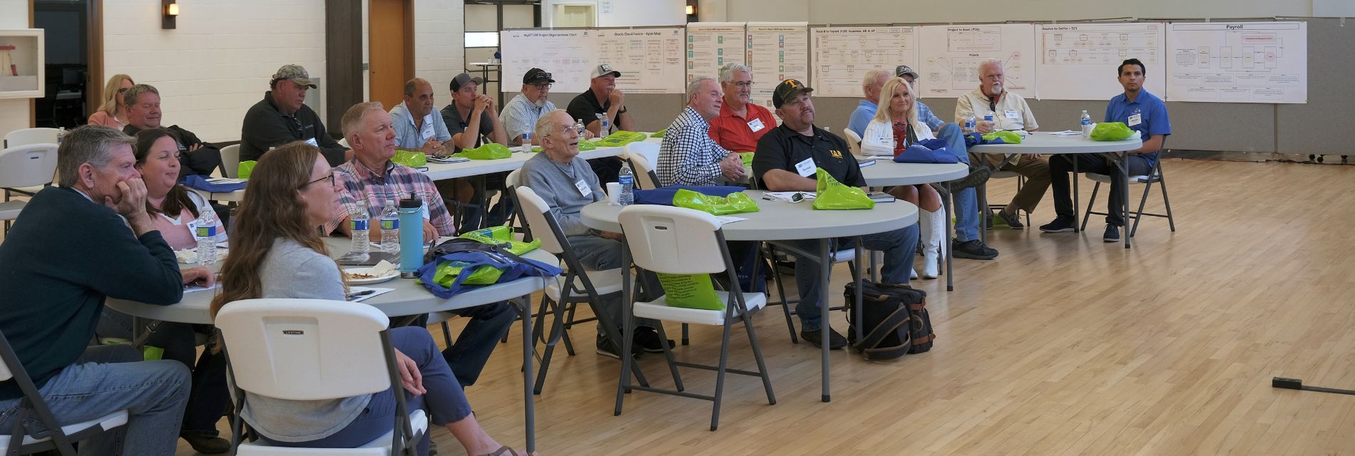 Audience sitting at several tables watch a presenter.