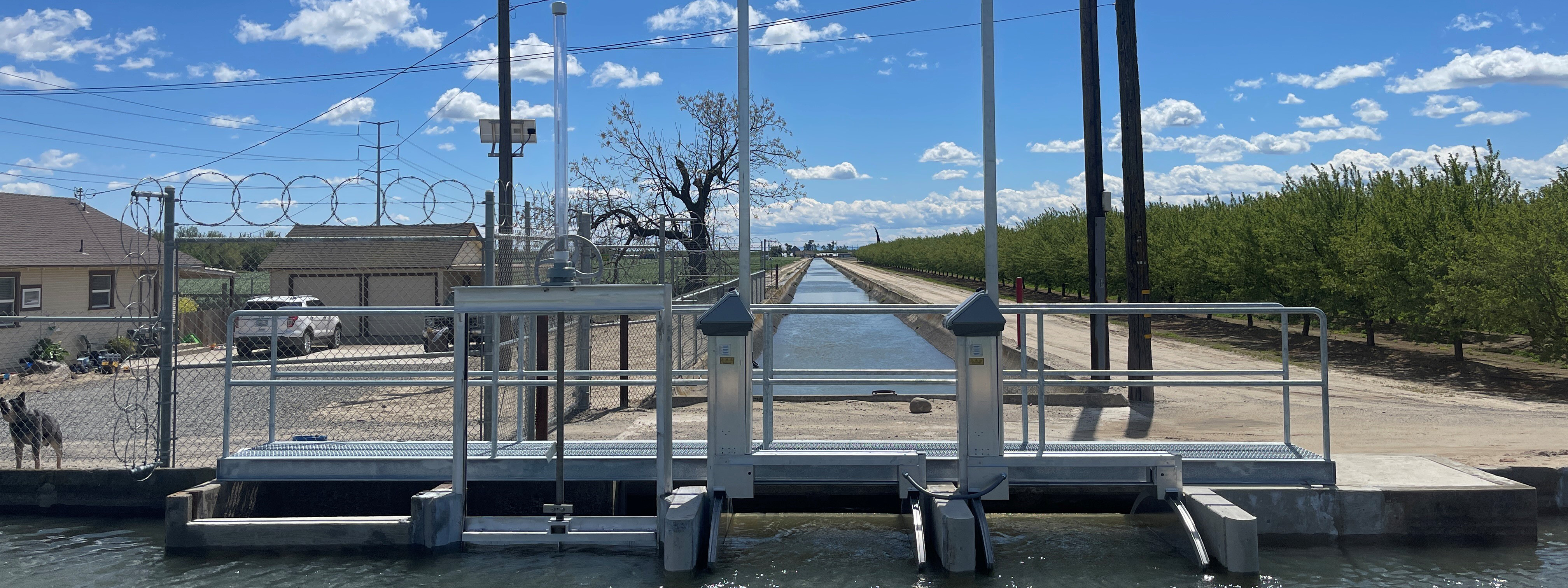 Automatic drop in irrigation canal with orchard in background.